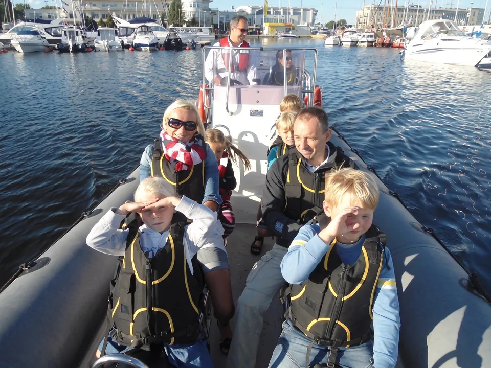 En familj med barn i flytvästar åker ribbåt i en marina i solsken