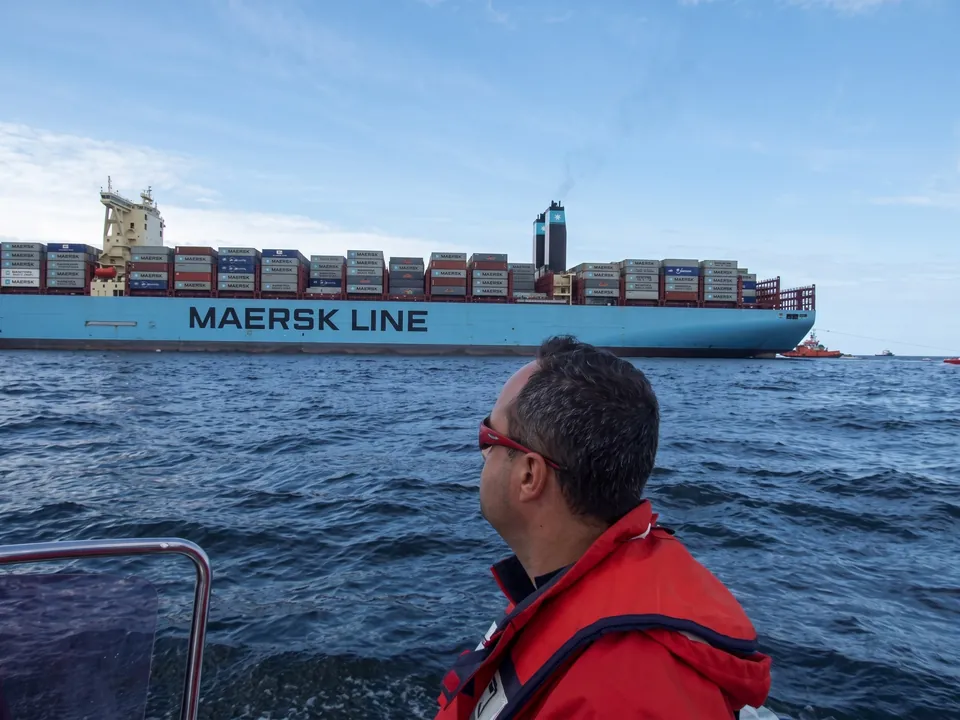 En man i flytväst på en båt tittar på ett containerfartyg från Maersk Line