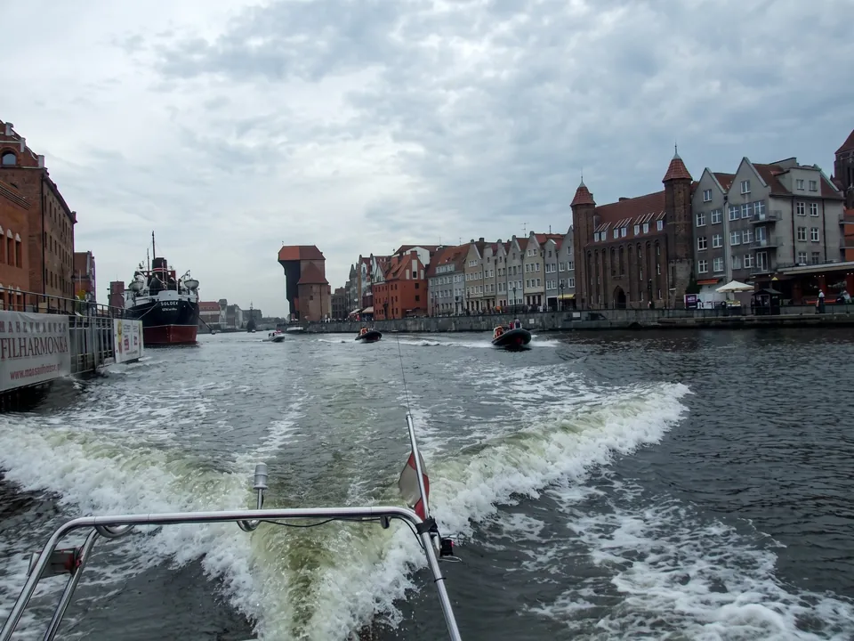 Kölvatten efter en båt på en flod bland historiska stadshus och en gammal kran
