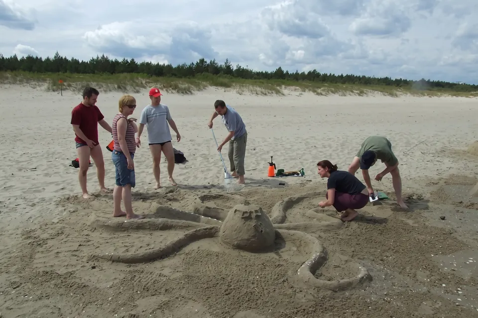 Participants sculpting a sand octopus on a wide beach