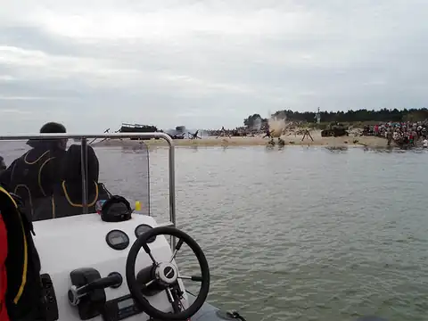 Console and steering wheel of a RIB, passengers in life jackets, the bay shore in the background