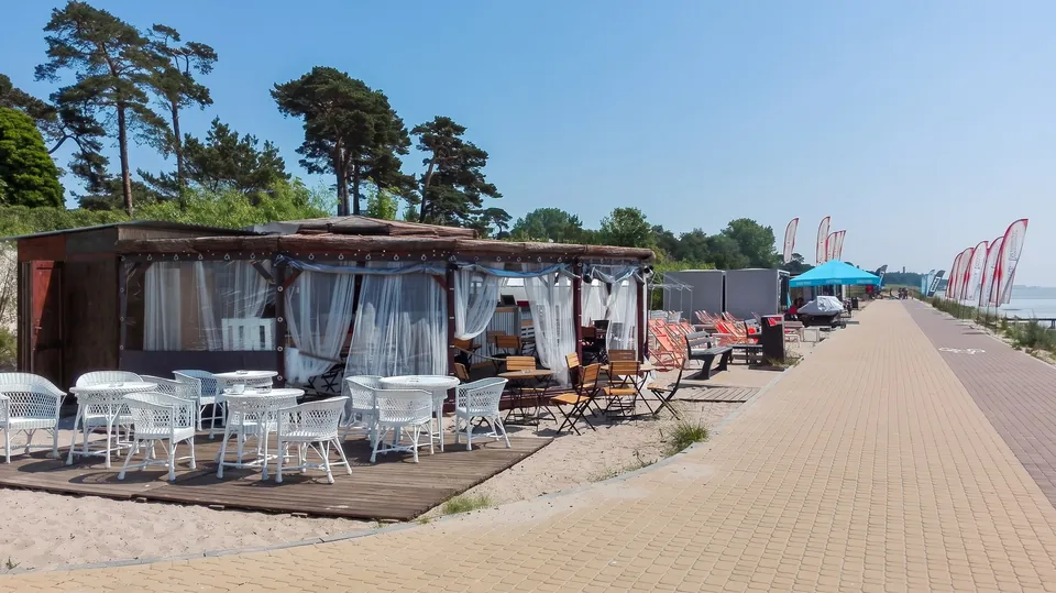 Kafé vid havet med vita korgmöbler intill strandpromenaden och solstolar