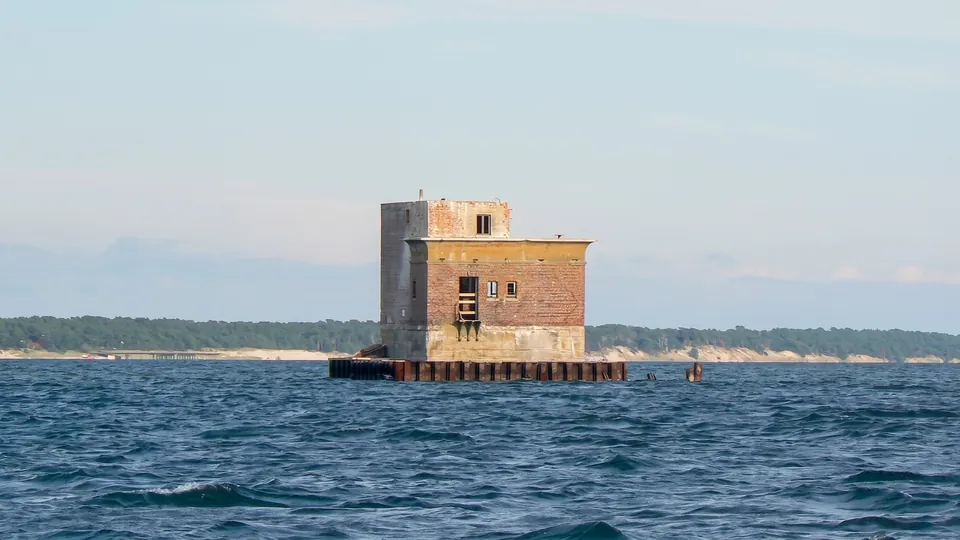 Tegelbyggnad på en betongplattform mitt i bukten, i bakgrunden en skogklädd strand