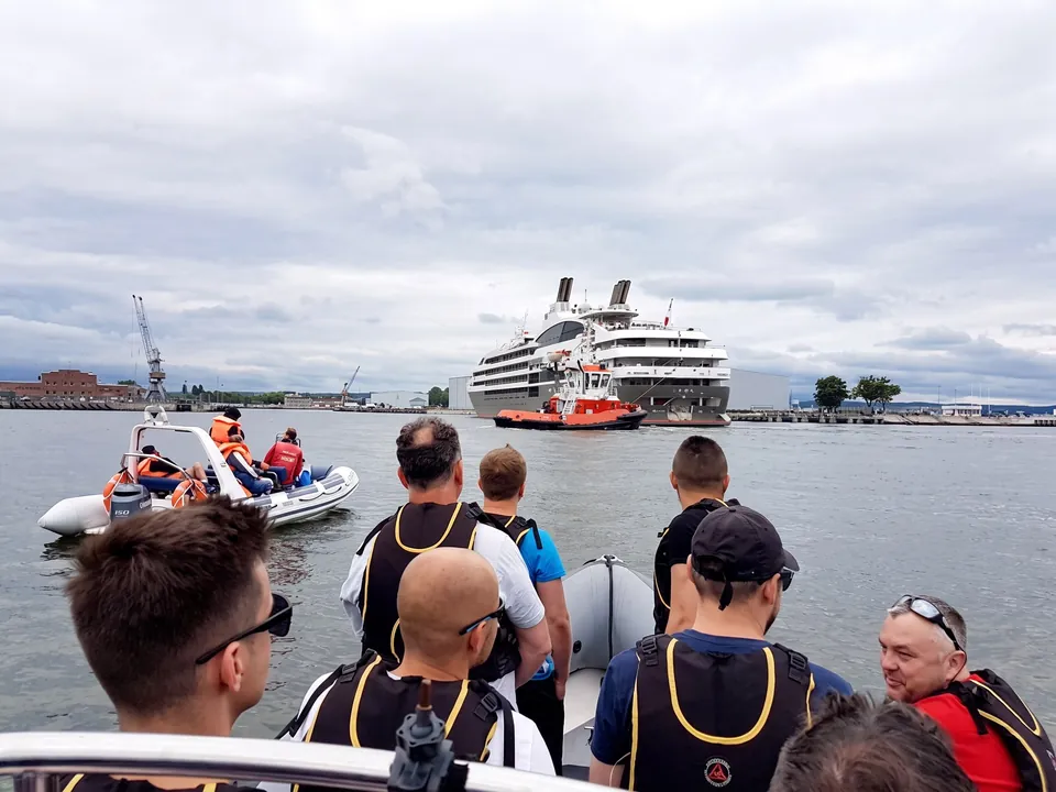Participants in life jackets on a RIB boat in the port, a large passenger ship ahead of them