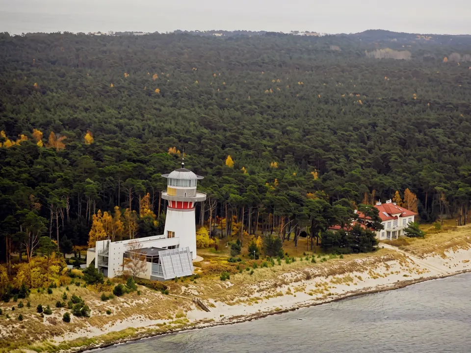 Lighthouse and buildings among the forest on the shore in Jurata from above