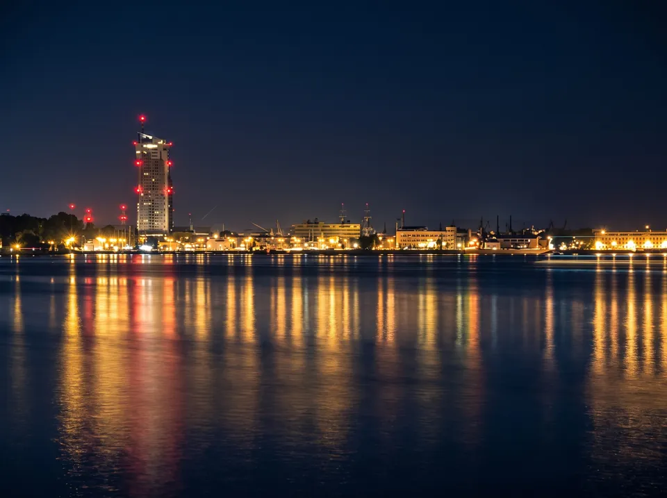 Nocna panorama Gdyni od strony morza, światła miasta odbite w spokojnej wodzie