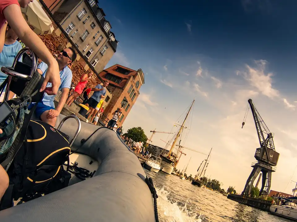 Vy från däcket på en ribbåt mot kajen, ett segelfartyg och en hamnkran i Gdańsk